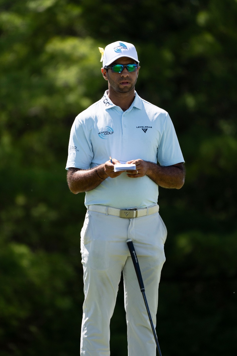 PGA Tour champion Aaron Rai reading his yardage book on the tee in a pale blue Levelwear polo and Me and My Golf cap at a professional golf tournament, sports photography by Toronto photographer Quinton Meyer