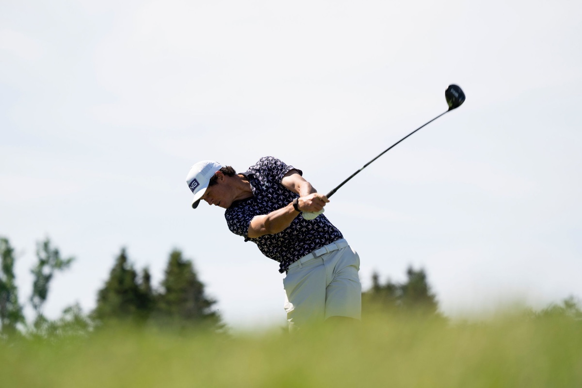 South African PGA Tour golfer Christo Lamprecht at the top of a powerful driver swing against a blue sky in a navy patterned polo and white PING cap, sports photography by Toronto photographer Quinton Meyer